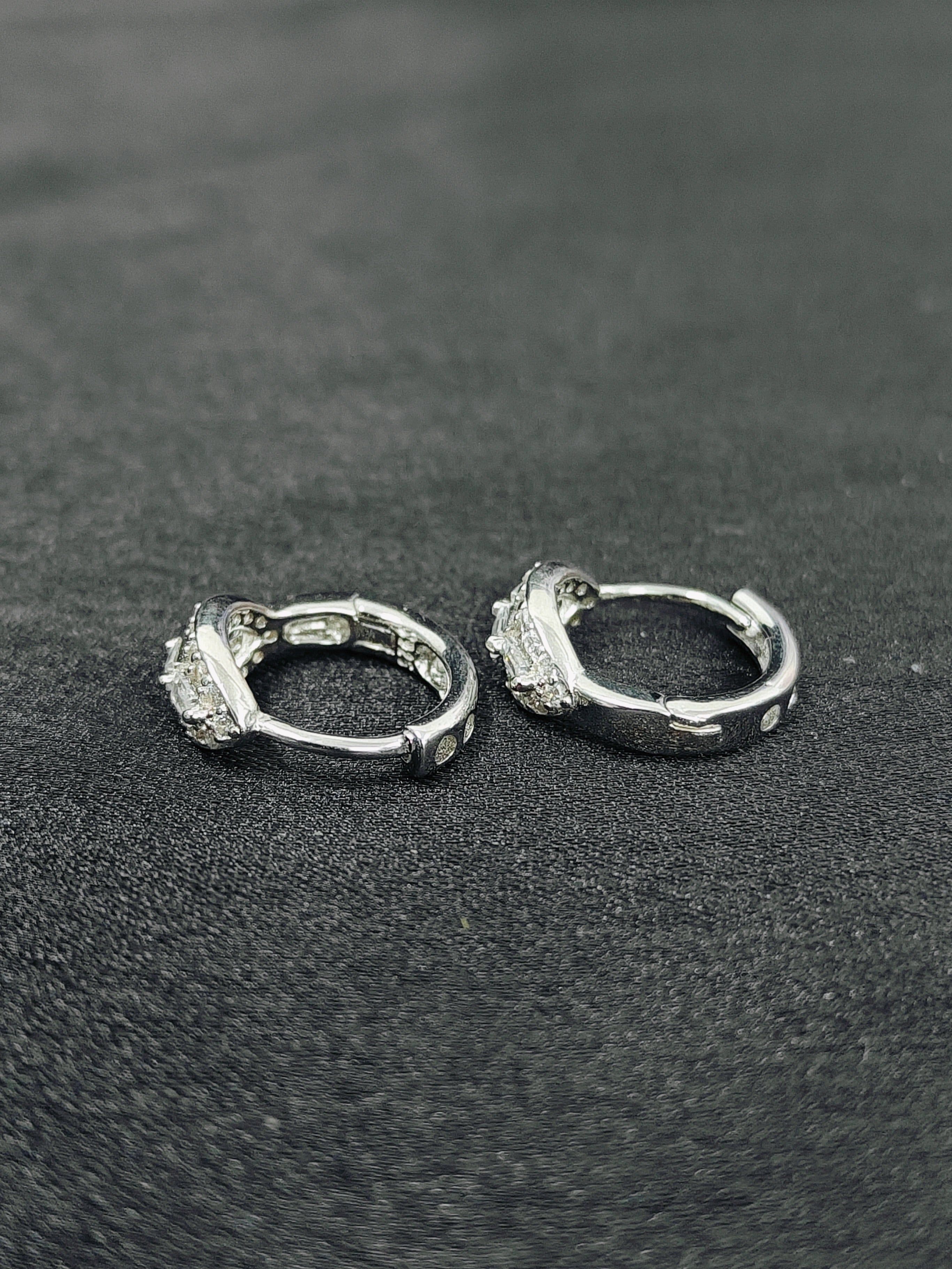 Pair of silver hoop earrings on a textured black surface